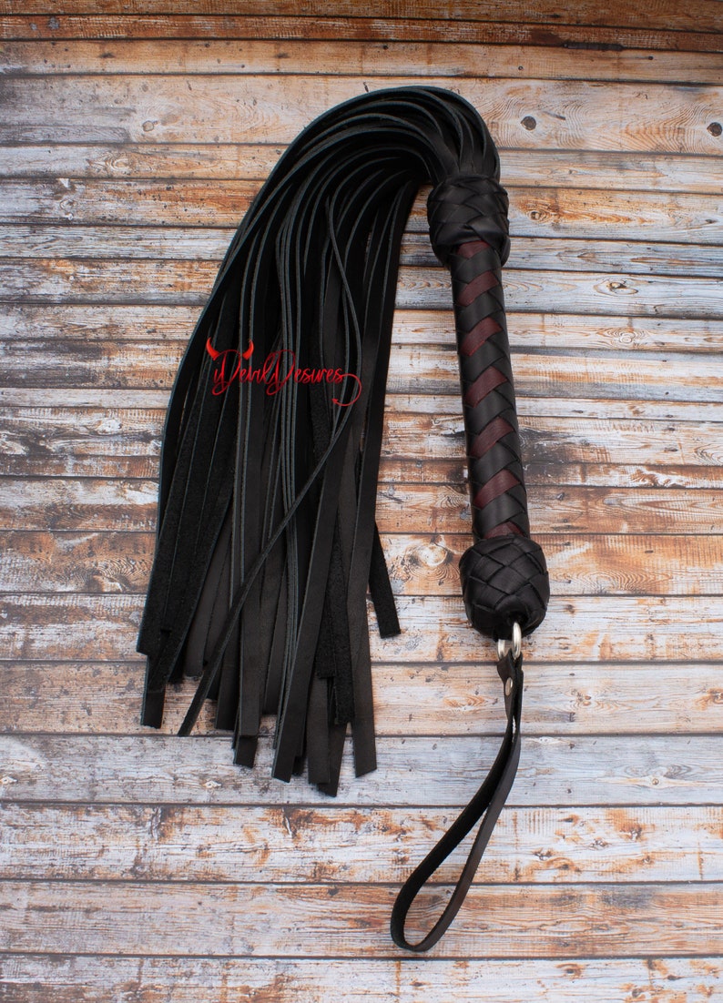 May include: A black leather whip with a braided handle and a long, fringed tail. The handle is made of dark brown leather with a red accent.