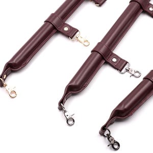 May include: Three burgundy leather straps with gold and silver metal clasps. The straps are designed for attaching to a harness or other leather goods.