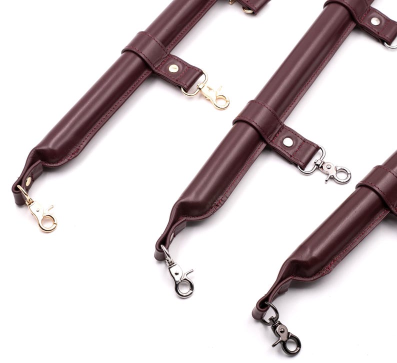 May include: Three burgundy leather straps with gold and silver metal clasps. The straps are designed for attaching to a harness or other leather goods.