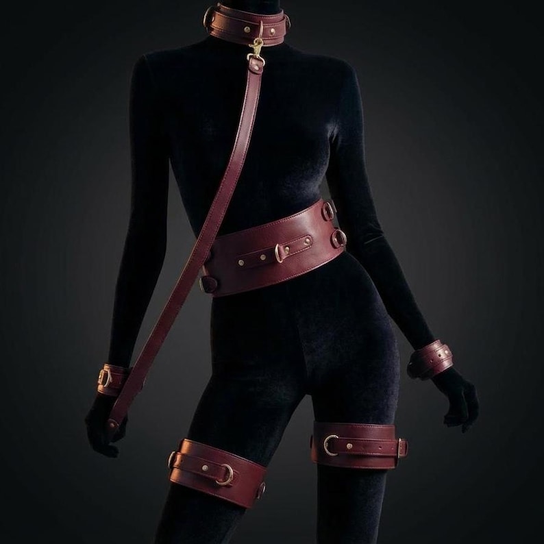 Luxury leather BDSM harness and bondage set worn on female body, burgundy restraint accessories with gold hardware sensual couple gift.