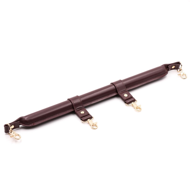 May include: A brown leather strap with three gold metal clasps and loops. The strap is designed to be used as a restraint.