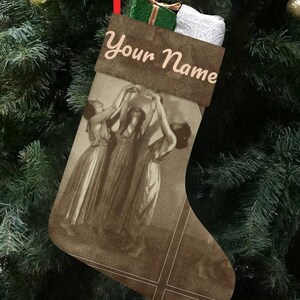 Puede incluir: Un calcetín navideño marrón con el texto "Your Name" en cursiva. El calcetín presenta una imagen en tonos sepia de mujeres bailando. El calcetín está lleno de regalos y cuelga de un árbol de Navidad decorado.