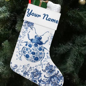 May include: White Christmas stocking with a blue and white beetle design and the text "Your Name". The stocking is decorated with blue floral patterns and is hanging on a Christmas tree.