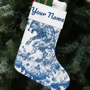Puede incluir: Calcetín navideño blanco con un diseño de lobo azul y detalles florales. La parte superior del calcetín es blanca con el texto "Your Name" en azul. Se adjunta una cinta roja para colgarlo. El calcetín está colgado en un árbol de Navidad.