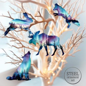 Peut inclure: Ensemble de cinq ornements en acier représentant un lapin, un renard, un élan et un loup. Chaque ornement présente un paysage coloré avec des arbres et un ciel vibrant. Les ornements sont suspendus à des crochets dorés.