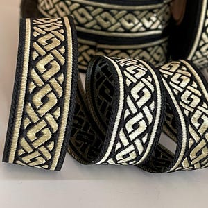 Peut inclure: Galon tressé noir et or avec un motif géométrique. Le galon est tissé avec un fil noir épais et un fil or plus fin.