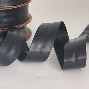 Può includere: Un rotolo di nastro in similpelle nero. Il nastro è arrotolato e ha una finitura liscia e lucida.