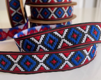 Könnte beinhalten: Rot-weiß-blaues gemustertes Band mit geometrischem Design. Das Band ist auf schwarzem Grund gewebt und zeigt ein sich wiederholendes Muster aus Rauten und X-Formen.