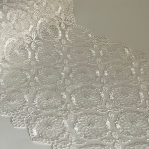 Puede incluir: Borde de encaje blanco con un delicado patrón floral. El encaje tiene un borde festoneado y es perfecto para agregar un toque de elegancia a cualquier proyecto.