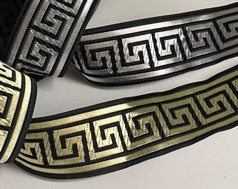 Könnte beinhalten: Drei verschiedene schwarze und weiße gemusterte Bandborten mit einem griechischen Schlüsselmuster. Die Borten haben silberne, goldene und beige Akzente.