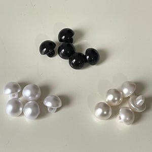 Peut inclure: Un assortiment de boutons en plastique noir et blanc. Les boutons sont ronds et ont une finition lisse. Il y a six boutons noirs et six boutons blancs.