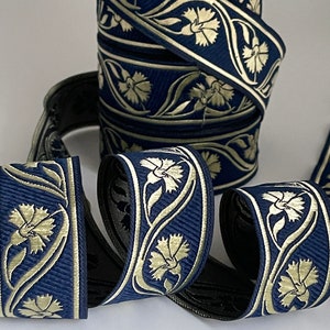 May include: A roll of navy blue and gold ribbon with a floral pattern. The ribbon is woven with a repeating design of stylized carnations and leaves.