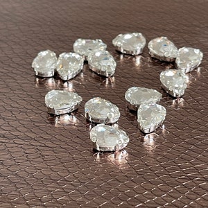 May include: A collection of clear teardrop-shaped rhinestones on a brown textured surface.