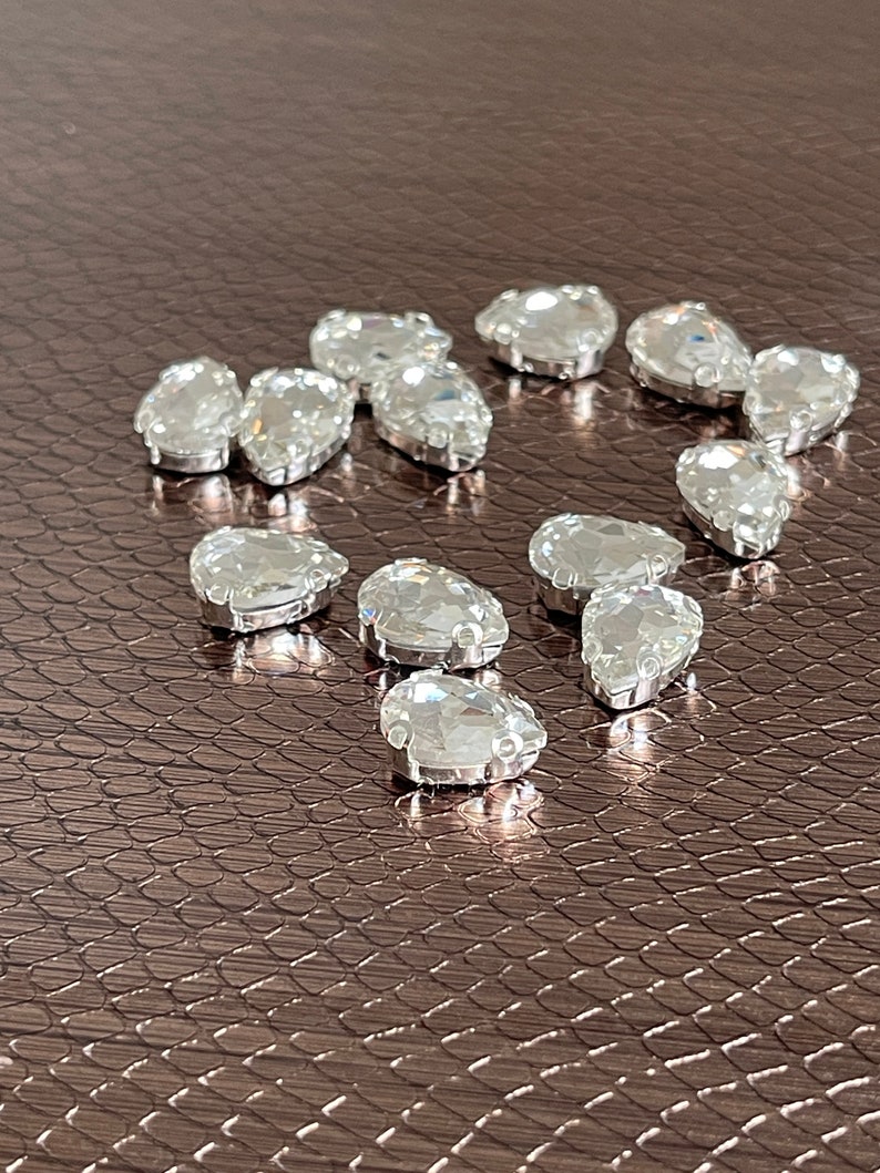 May include: A collection of clear teardrop-shaped rhinestones on a brown textured surface.