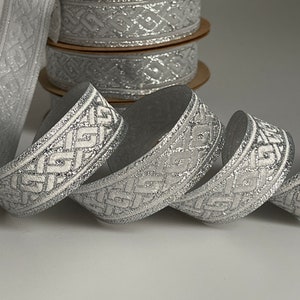May include: Silver ribbon with a white geometric pattern. The ribbon is rolled up and has a sparkly finish.