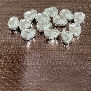 May include: A group of clear teardrop-shaped rhinestones on a brown textured surface.