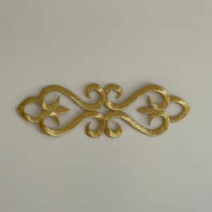 Peut inclure: Garniture brodée dorée avec un motif décoratif orné. Cette garniture est parfaite pour ajouter une touche d'élégance aux vêtements, aux objets artisanaux et aux projets de décoration intérieure.