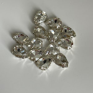 May include: A group of clear pear-shaped rhinestones with silver settings.