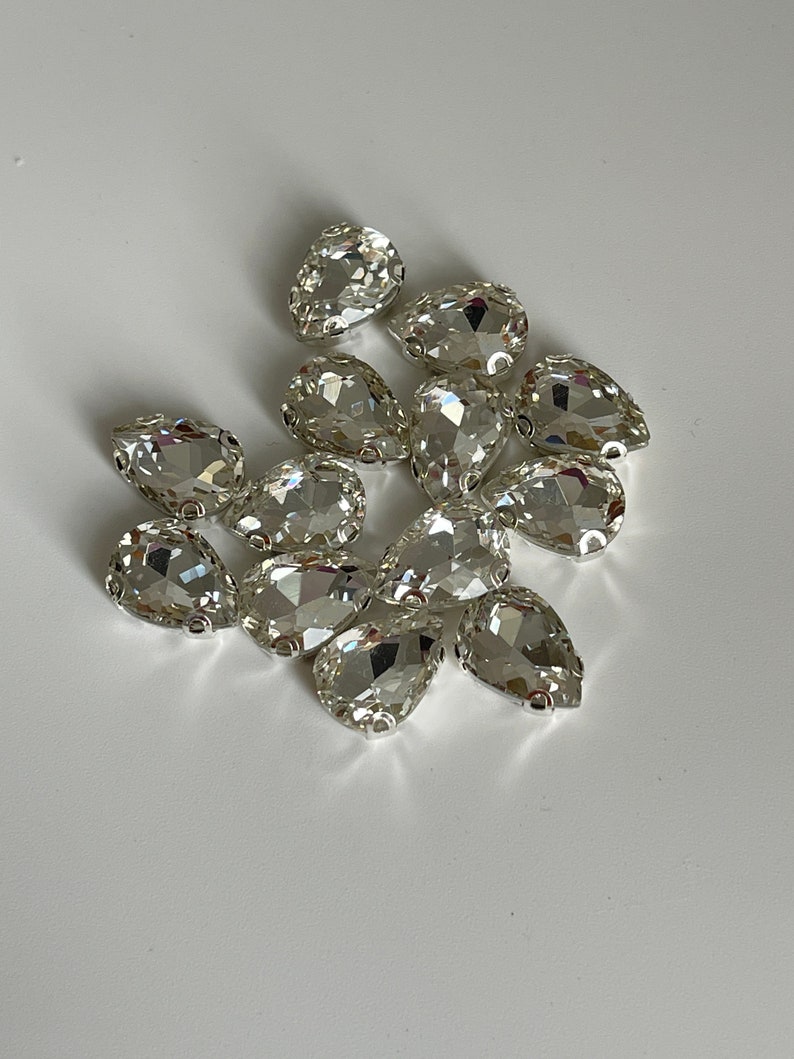 May include: A group of clear pear-shaped rhinestones with silver settings.