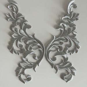 Può includere: Due applicazioni in tessuto ricamate decorative di colore argento in un design floreale.