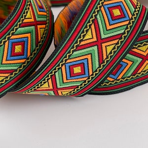 Op de afbeelding: Veelkleurige geweven trim met een geometrisch patroon met rode, groene, gele, blauwe en oranje vierkanten en driehoeken. De trim heeft een zwarte achtergrond.