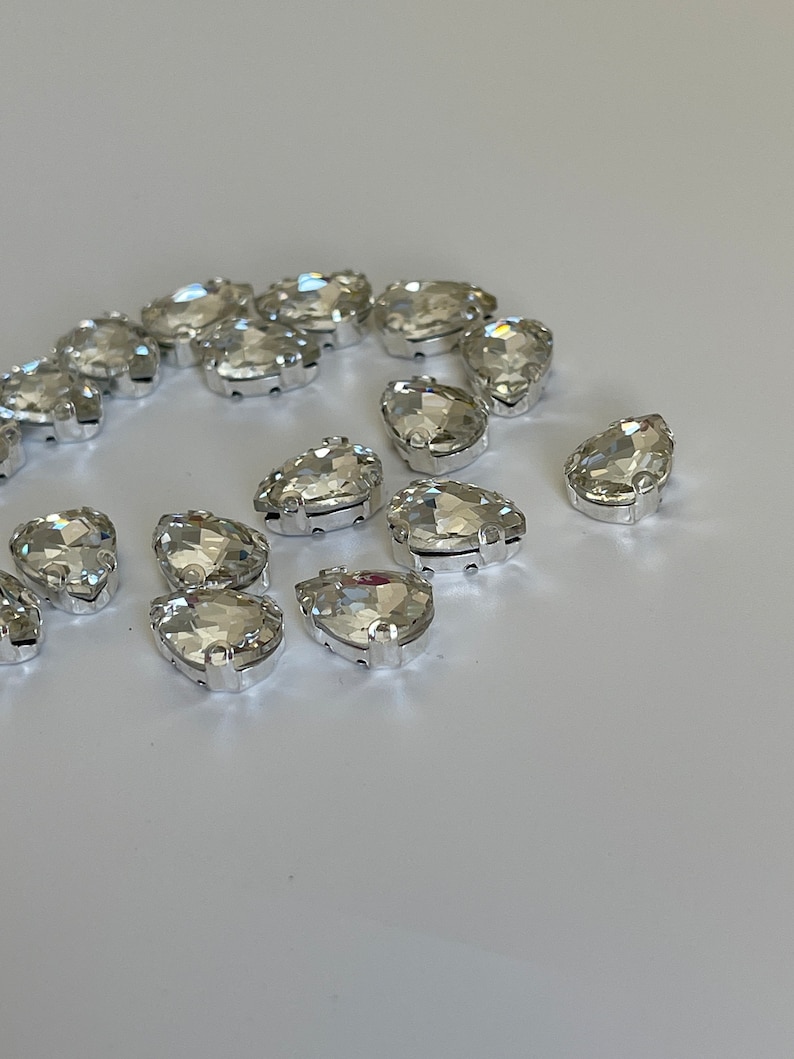May include: A group of clear crystal teardrop-shaped rhinestones with silver settings.