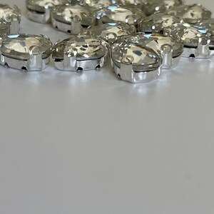 May include: A group of clear oval-shaped rhinestones with silver settings. The rhinestones are arranged in a loose circle.