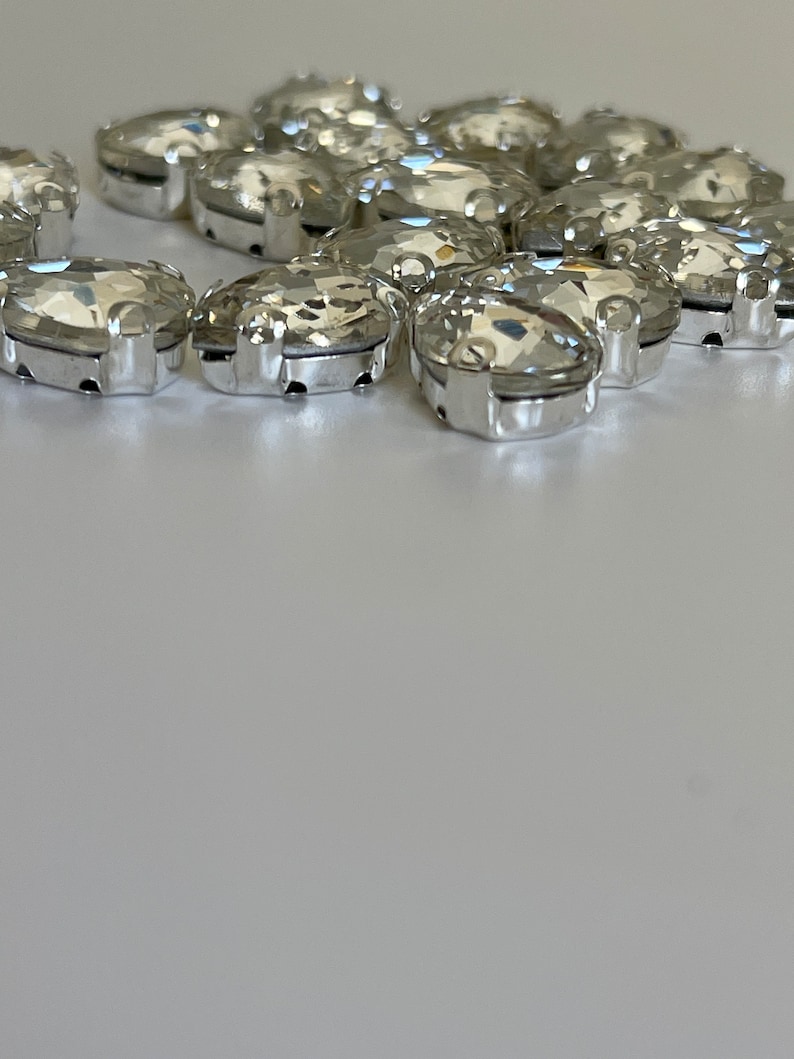 May include: A group of clear oval-shaped rhinestones with silver settings. The rhinestones are arranged in a loose circle.