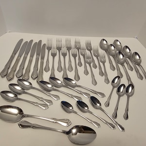 May include: A set of stainless steel cutlery, including forks, knives, and spoons. The cutlery has an ornate design with a floral pattern.