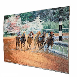 May include: A tapestry depicting a horse race with six horses and riders in a close finish. The horses are brown and black, and the riders are wearing colorful jockey silks. The race is taking place on a dirt track with a green background of trees and flowers. The tapestry is signed "Mary S. Russell".