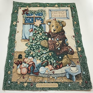 Puede incluir: Un tapiz con un oso de peluche marrón decorando un árbol de Navidad con adornos y luces. El tapiz tiene un borde verde con un patrón dorado y blanco. El texto "HO-HO-OH-NO!" se muestra sobre el oso. La parte inferior del tapiz dice "BOYDS BEARS & FRIENDS TM".