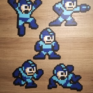 Könnte beinhalten: Fünf Pixel-Art-Figuren von Mega Man, einem Videospielcharakter, in verschiedenen Posen. Die Figuren sind aus blauen, hellblauen und weißen Perlen gefertigt.