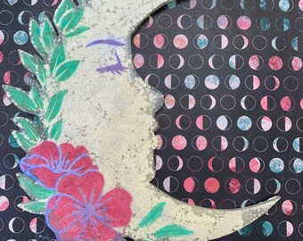 Pode incluir: Uma lua crescente branca com um design floral e um rosto pintado. A lua é decorada com folhas verdes e flores cor-de-rosa. O fundo é um padrão preto e branco de meias luas.