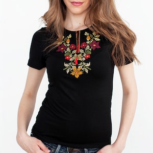 May include: A black short-sleeved shirt with embroidered flowers in red, orange, yellow, and green. The shirt is worn with blue jeans.