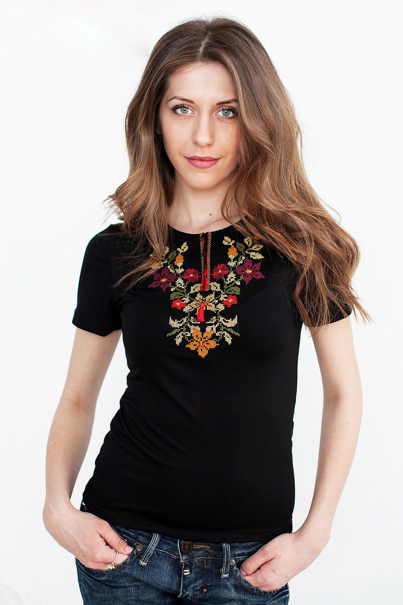 May include: A black short-sleeved shirt with embroidered flowers in red, orange, yellow, and green. The shirt is worn with blue jeans.