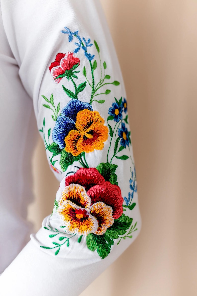 Close-up detail of a white 3/4 length sleeve showcasing beautiful machine embroidery of colorful pansies and wildflowers in Spanish style.