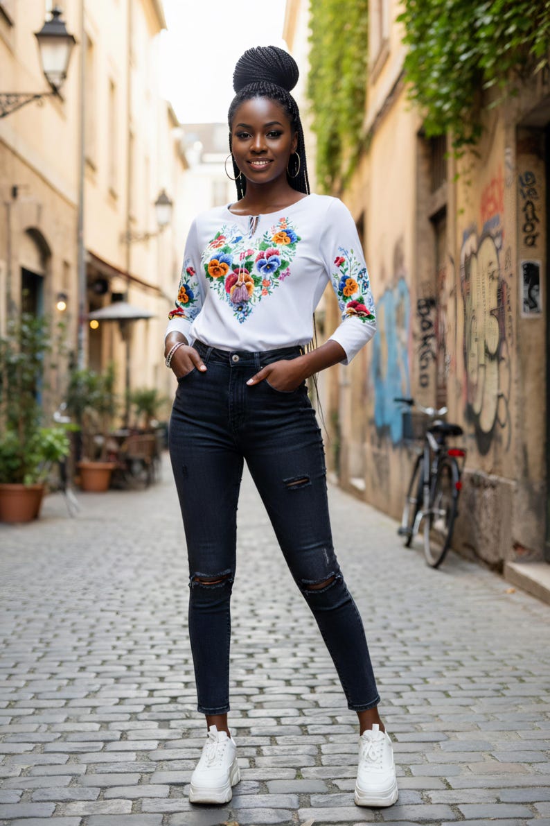 Full length fashion shot of a woman walking in the city, styling a white floral boho top with dark jeans and sneakers.