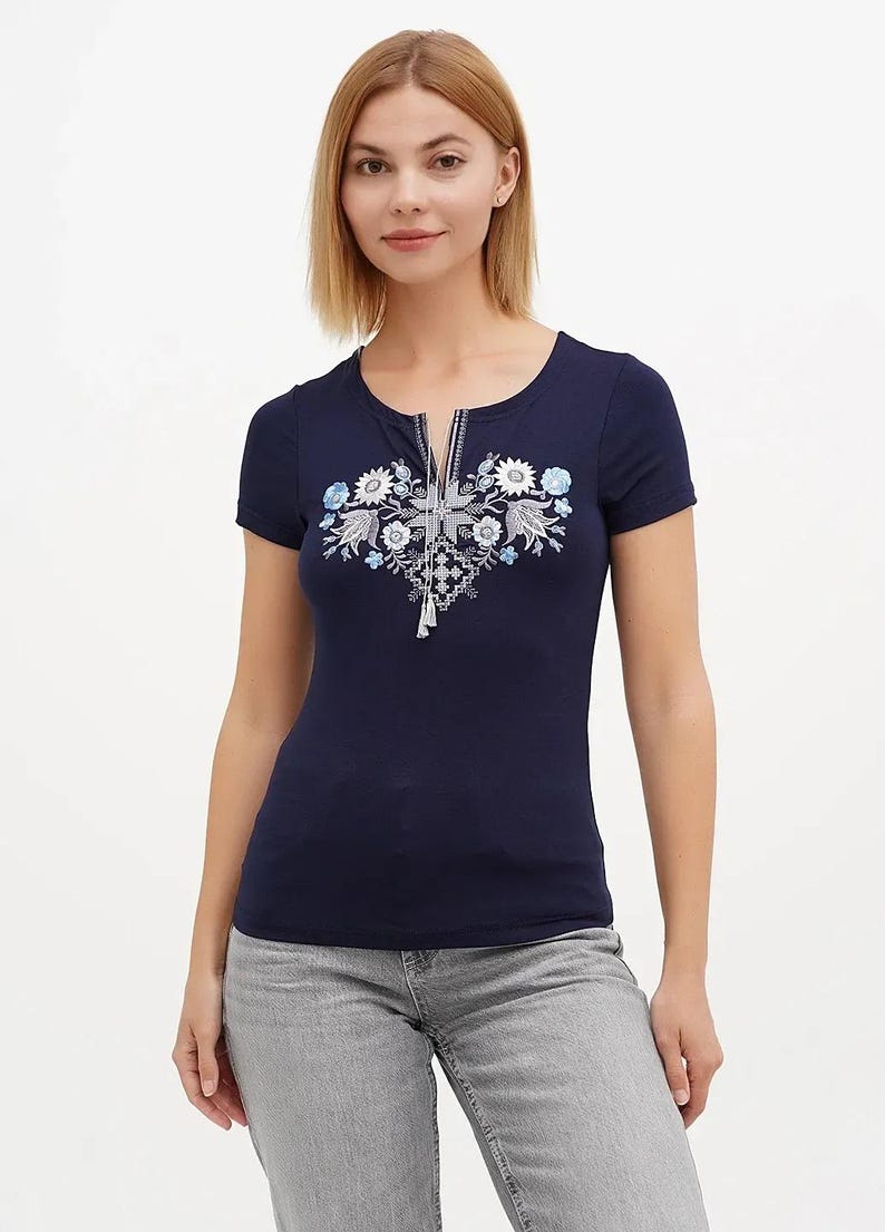 May include: Navy blue short-sleeve shirt with a floral embroidery design on the front. The shirt has a zipper detail at the neckline and a tassel. The embroidery features white and light blue flowers.