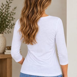 Back view of a blonde model wearing a fitted white 3/4 sleeve embroidered top, highlighting the garment's comfortable and flattering fit.