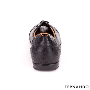 以下が含まれることがあります： ヘビ柄の黒い革靴。靴はレースアップクロージャーと丸みを帯びたつま先を持っています。