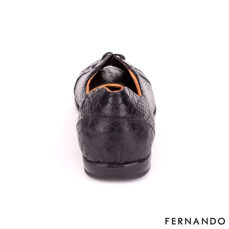 以下が含まれることがあります： ヘビ柄の黒い革靴。靴はレースアップクロージャーと丸みを帯びたつま先を持っています。