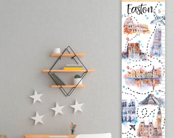 Puede incluir: Un gráfico de crecimiento de madera blanca con un diseño de acuarela que presenta monumentos de todo el mundo. El gráfico está etiquetado como "Easton" y tiene una escala en pulgadas de 20 a 60. El gráfico está colgado en una pared con una varilla de madera.
