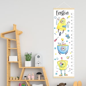 Può includere: Un'altezza per bambini con illustrazioni di robot gialli e blu, con il nome "Easton". L'altezza misura fino a 147 cm, con un gancio di legno. Il design include strumenti e stelle.