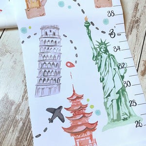 Puede incluir: Un medidor de altura de lienzo blanco con ilustraciones en acuarela de monumentos mundiales, incluyendo la Estatua de la Libertad, la Torre de Pisa y una pagoda. Una ruta de vuelo en l&iacute;nea discontinua negra conecta los sitios, con marcas en pulgadas.