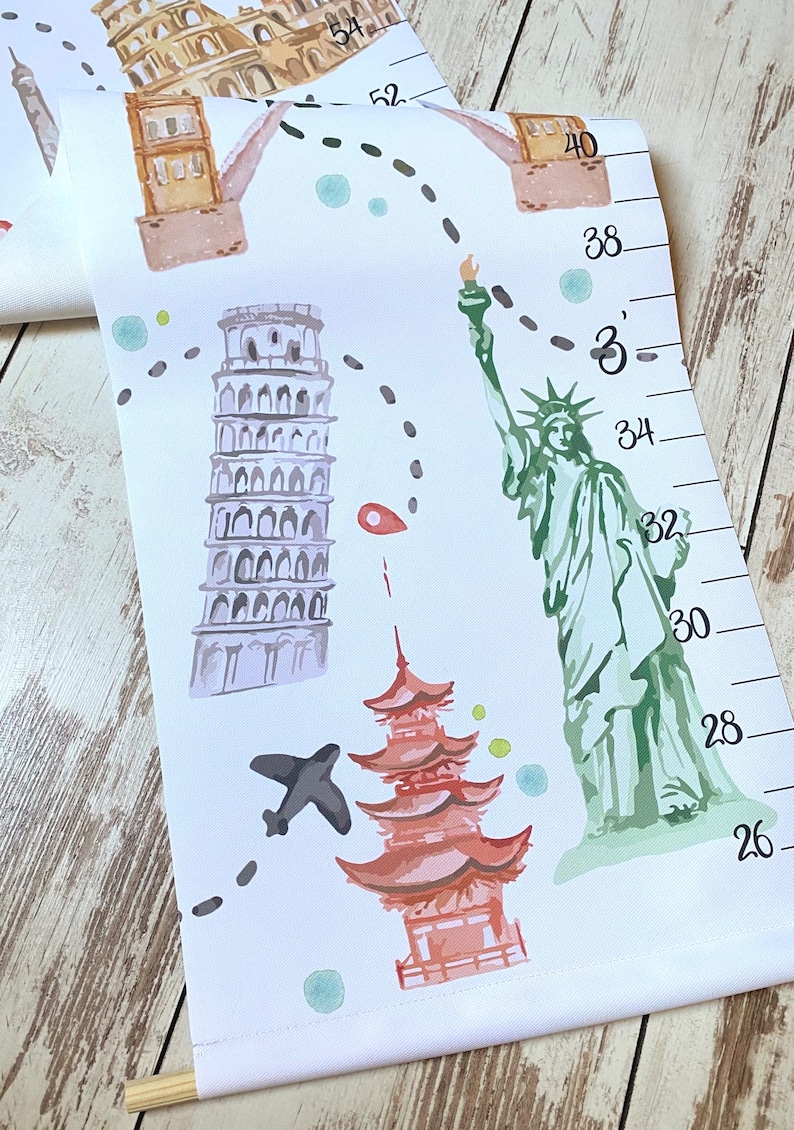 Puede incluir: Un medidor de altura de lienzo blanco con ilustraciones en acuarela de monumentos mundiales, incluyendo la Estatua de la Libertad, la Torre de Pisa y una pagoda. Una ruta de vuelo en l&iacute;nea discontinua negra conecta los sitios, con marcas en pulgadas.