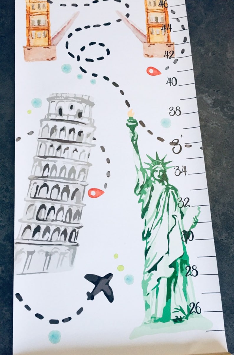 Puede incluir: Un medidor de altura blanco con ilustraciones en acuarela de la Torre de Pisa, la Estatua de la Libertad y un puente. Un camino de viaje en l&iacute;nea negra discontinua conecta los monumentos, junto a un peque&ntilde;o avi&oacute;n y marcas numeradas en cent&iacute;metros.
