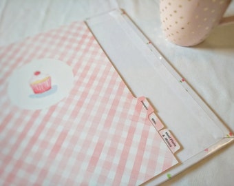 Puede incluir: Un archivador de recetas de gingham rosa y blanco con pestañas etiquetadas como "Postres", "Varios" y "Planes de comidas y menús".