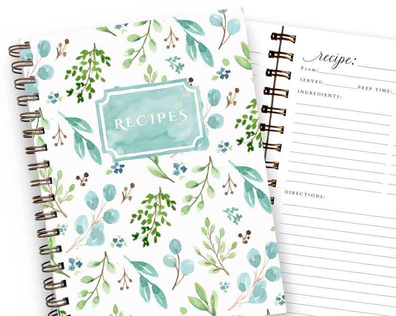 May include: A spiral-bound recipe journal with a watercolor floral design. The cover features a teal label with the word "RECIPES" and is adorned with green and blue leaves. The open page displays a recipe template with prompts for ingredients and directions.