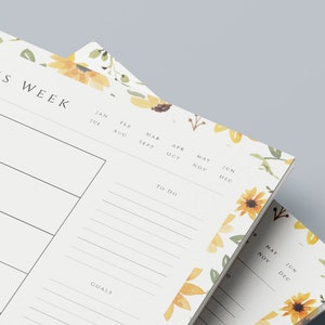 May include: Two white weekly planner pads with a floral design featuring sunflowers and green leaves. The top pad has the text "THIS WEEK" and includes sections for "To Do" and "Goals". The bottom pad has a calendar with the months of May, June, November, and December.