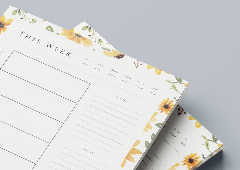 May include: Two white weekly planner pads with a floral design featuring sunflowers and green leaves. The top pad has the text "THIS WEEK" and includes sections for "To Do" and "Goals". The bottom pad has a calendar with the months of May, June, November, and December.